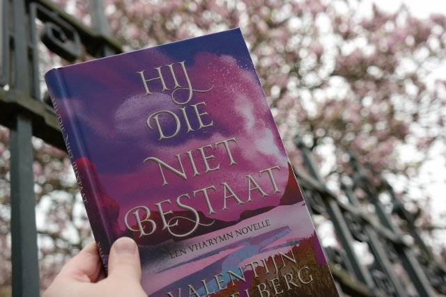 Boek Hij die niet bestaat van Valentijn Ringelberg met op de achtergrond een roze bloesemboom.